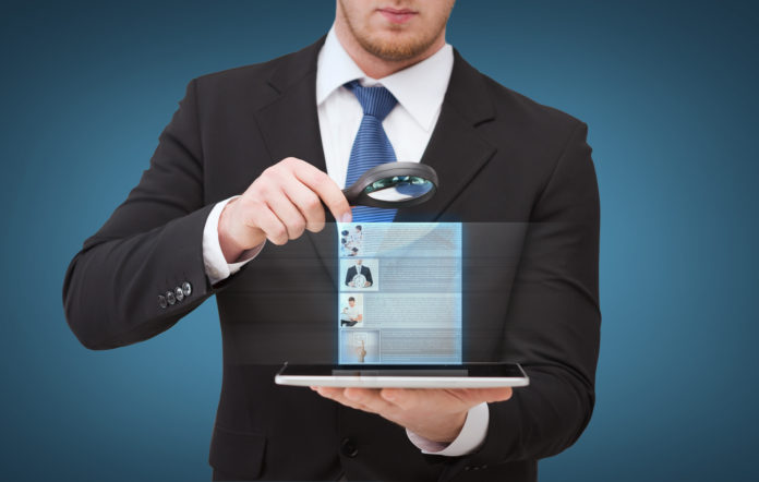 businessman hand holding magnifier over tablet pc